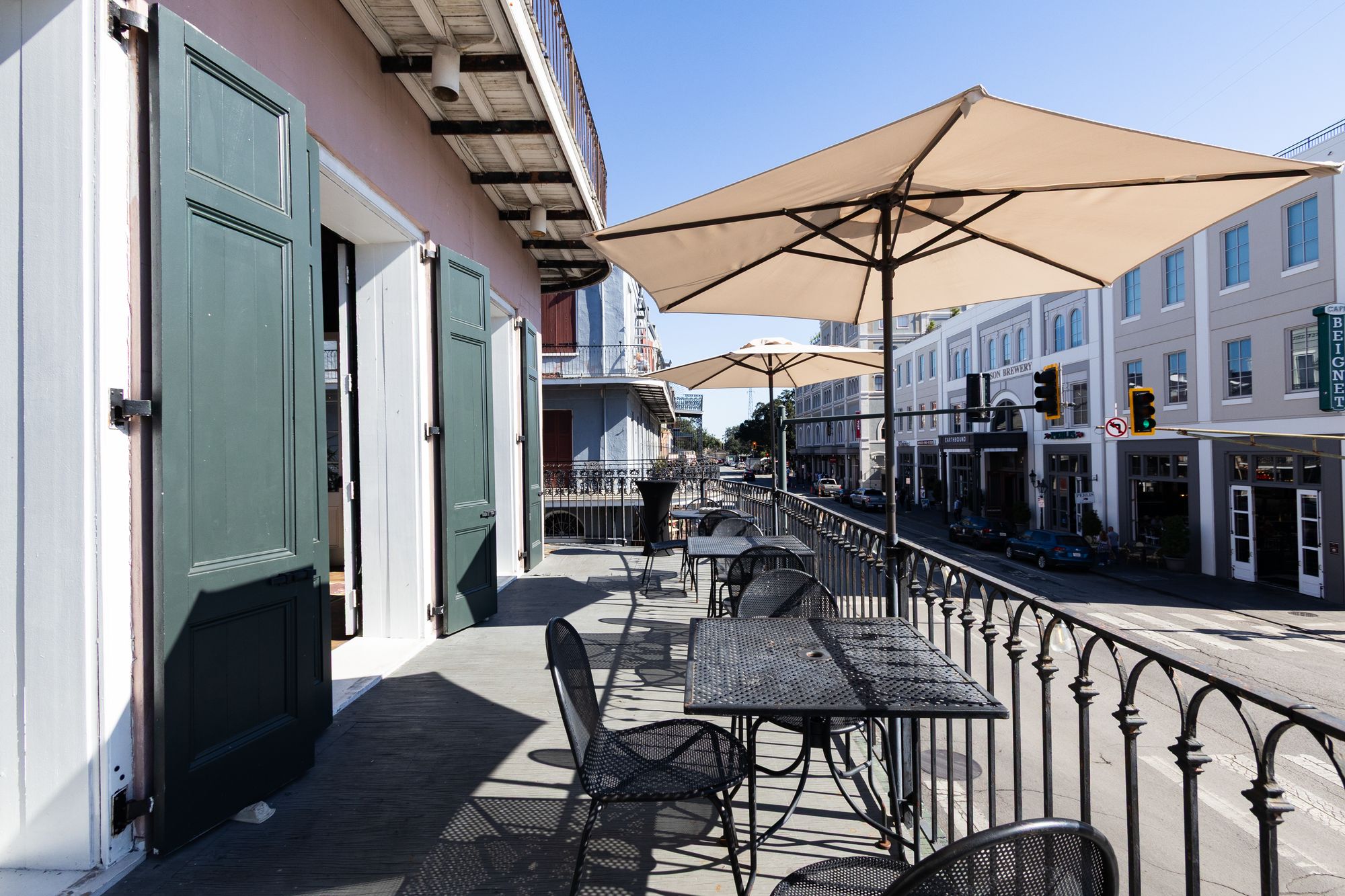 Second-floor balcony with umbrella-shaded bistro tables above Decatur Street