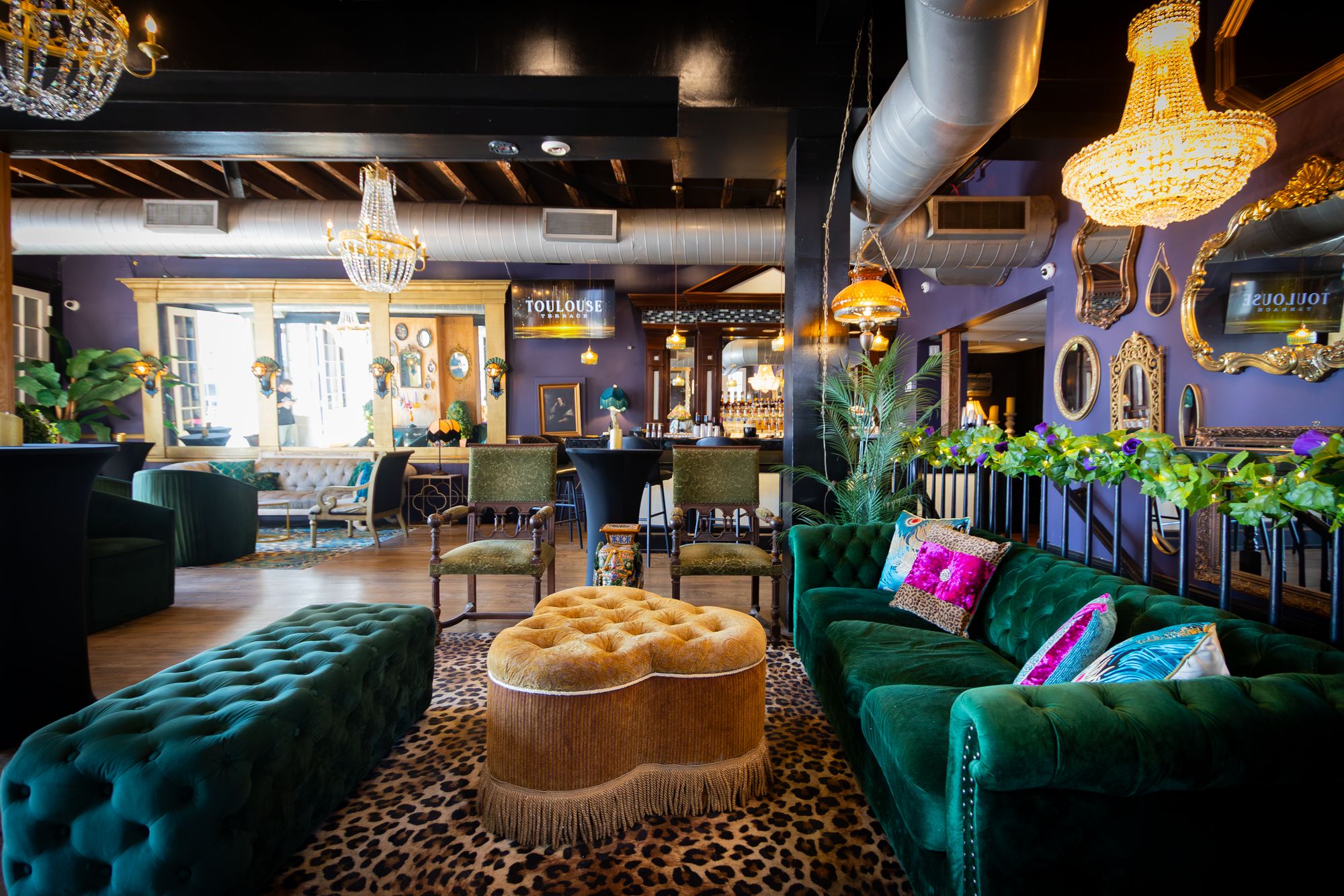 Green velvet sofa with jewel-tone pillows and a tufted ottoman beneath a chandelier