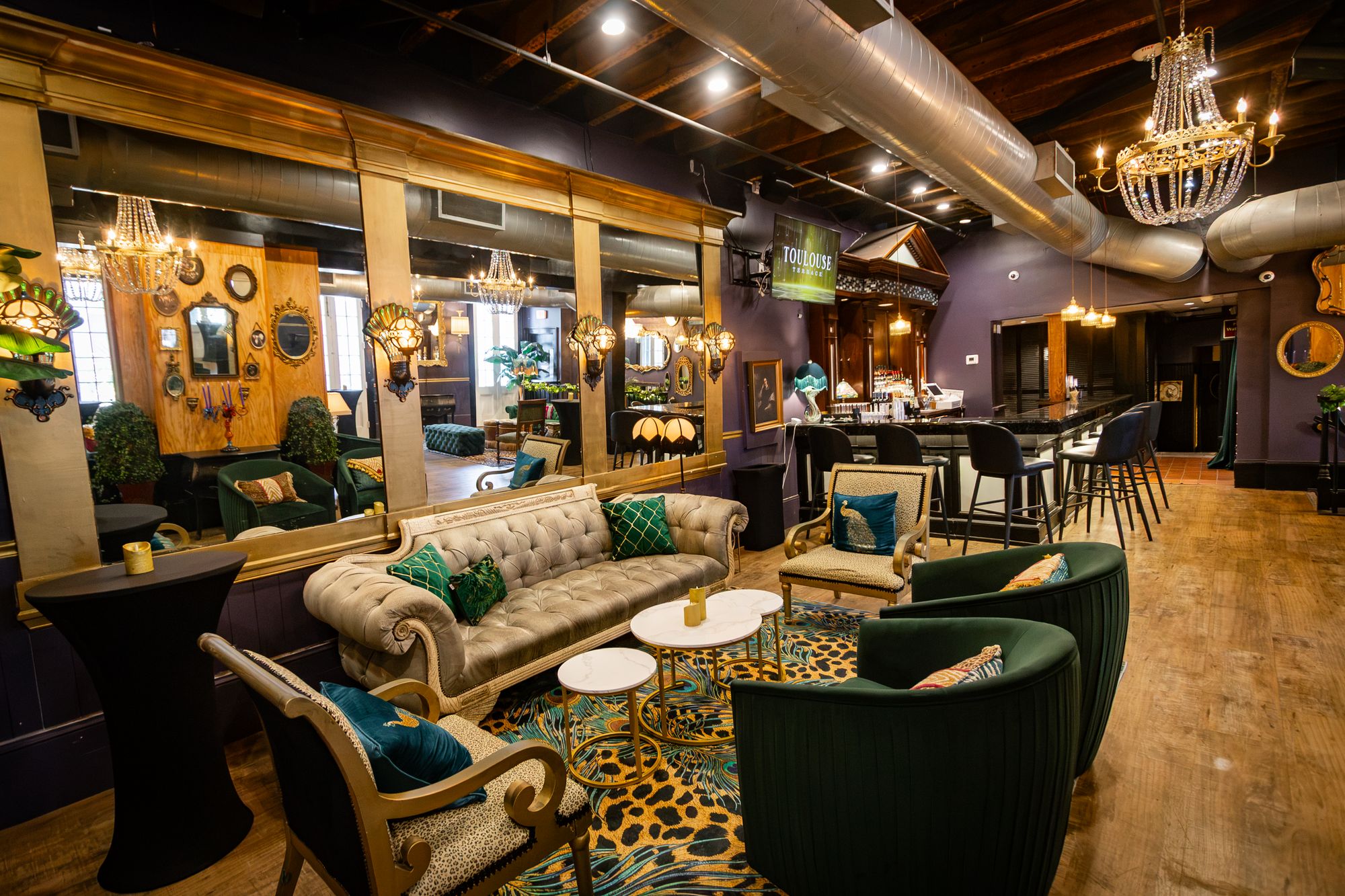 Wide view of the lounge with tufted sofa, velvet chairs and the bar beyond