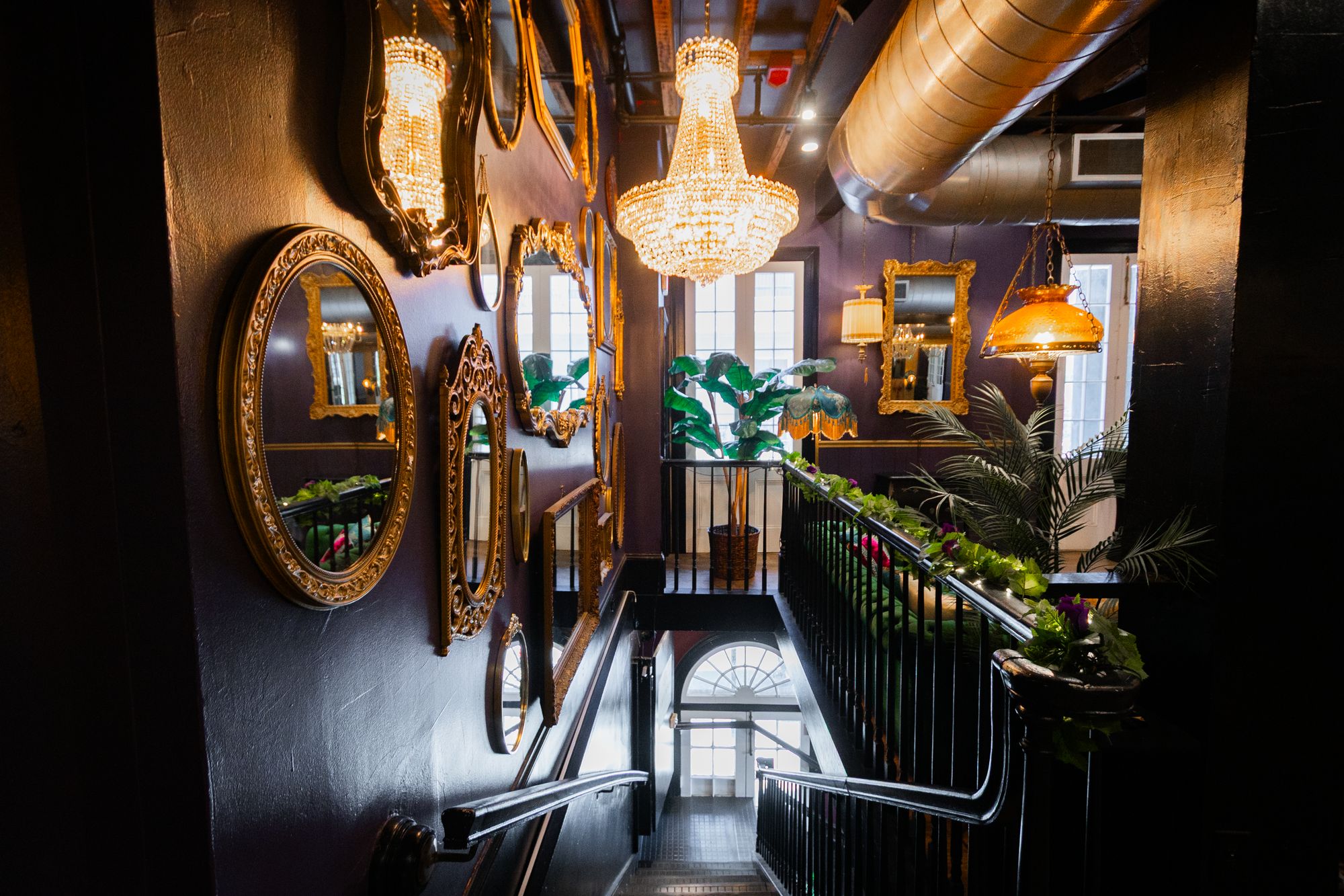 Staircase entrance framed by gilded mirrors and a crystal chandelier